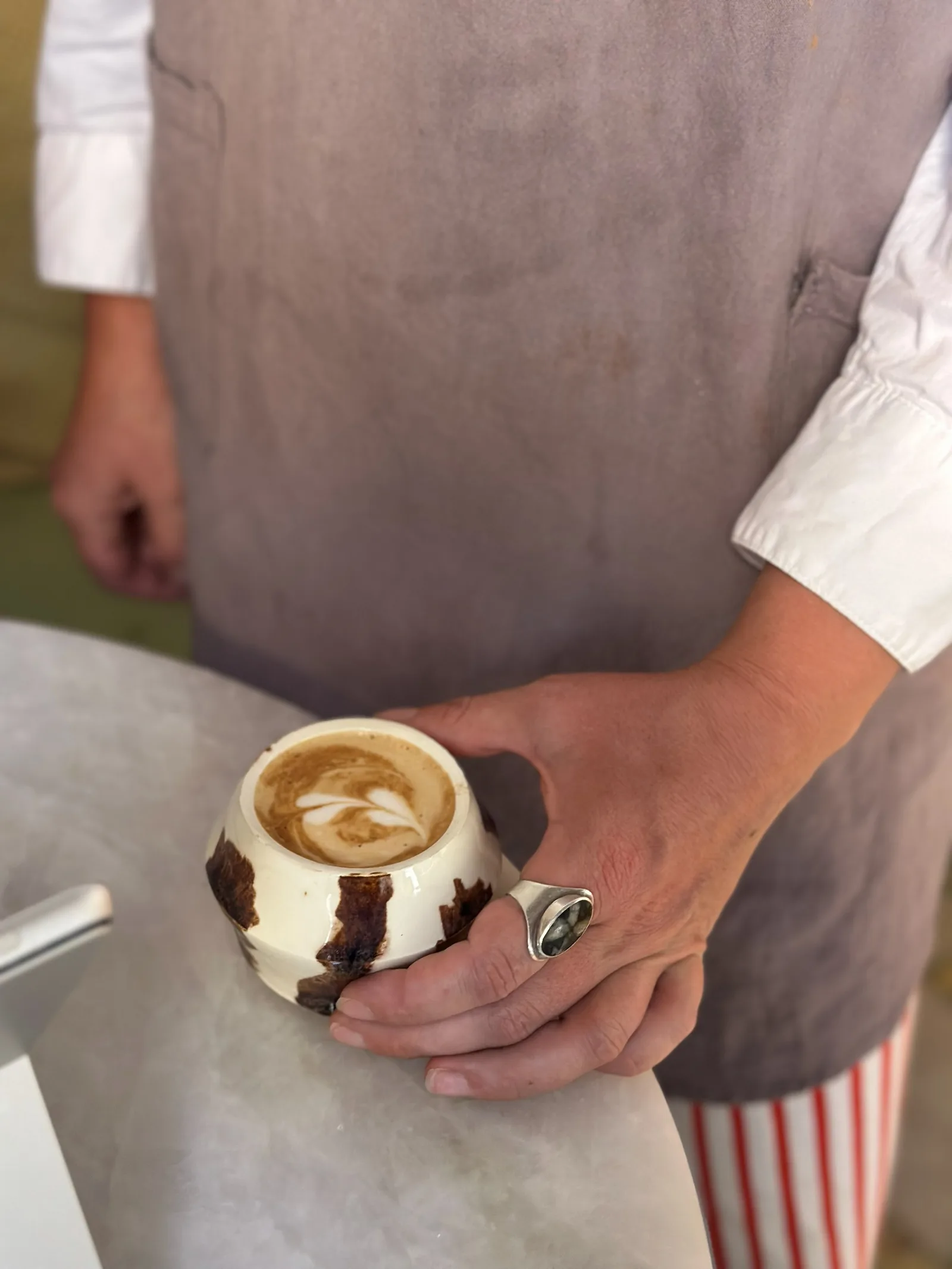 Un barista con mandil sostiene una taza con arte latte.