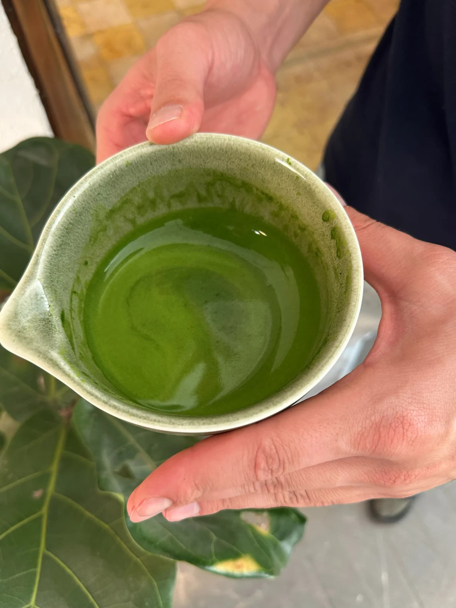 Manos sosteniendo una taza de matcha recién preparado.