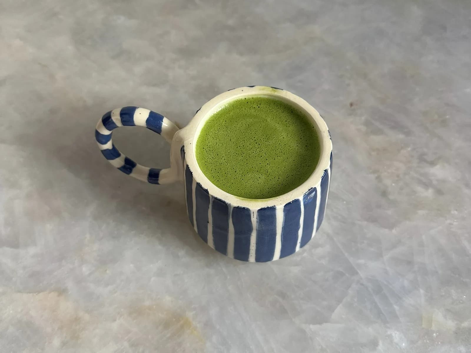 Taza de barro rayada con matcha, vista desde arriba sobre mármol.